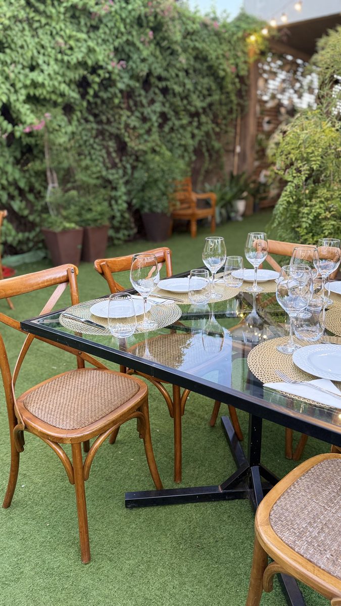 Mesa posta no jardim com taças e cadeiras de palhinha