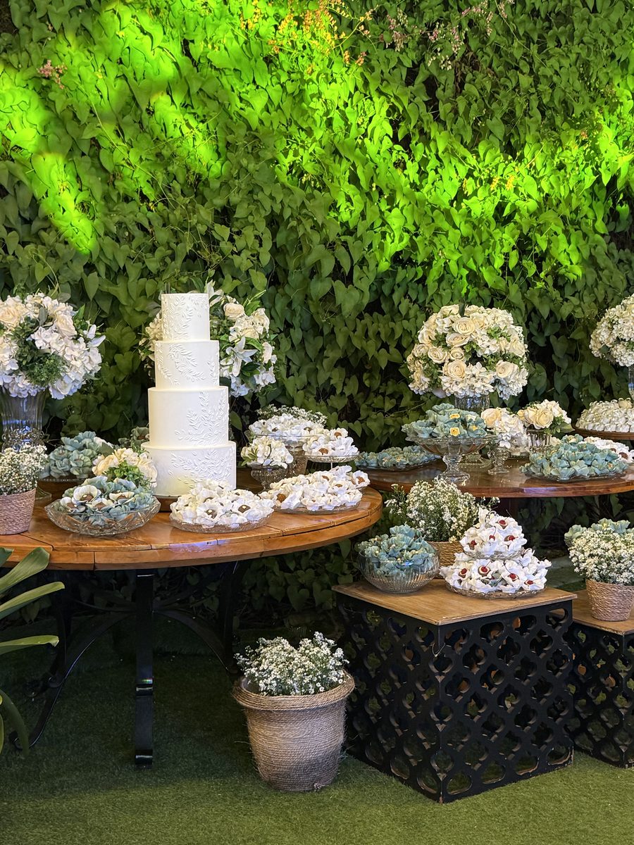 Bolo branco com mesa de doces e parede verde