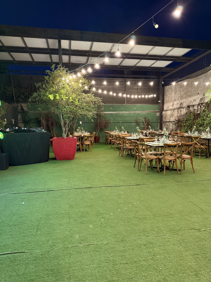 Salão amplo com luzes pendentes e mesas para evento
